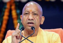 Yogi Adityanath Slams Films for Glorifying Dacoits, Warns of Impact on Youth A saffron-robed Hindu monk with a tilak on his forehead speaking at a podium with two microphones, raising his index finger while addressing an audience, with floral decorations in the background.