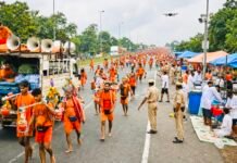 TheNews21 Explainer: Trucks, Bhajans and Bare Feet: How the Kanwar Yatra Became One of India’s Biggest Religious Gatherings Kanwariyas in saffron walking barefoot with decorated kanwars along a highway as police manage traffic and roadside camps serve pilgrims.
